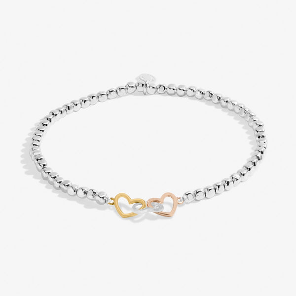 Joma Jewellery beaded bracelet with three interlinked hearts in silver, gold and rose gold presented on a blush pink sentiment card.