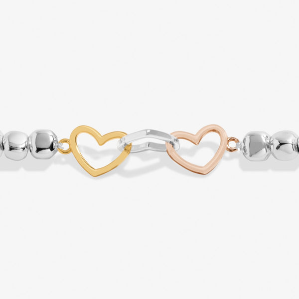 Joma Jewellery beaded bracelet with three interlinked hearts in silver, gold and rose gold presented on a blush pink sentiment card.