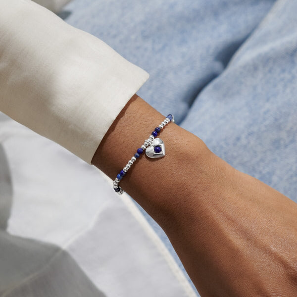 Joma Jewellery stretch beaded birthstone bracelet with blue semi-precious gemstones and a silver plated hanging heart charm.